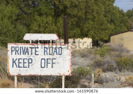 Rusty Warning sign for Limited or restricted access on private road to private property, with blurred background of buildings.