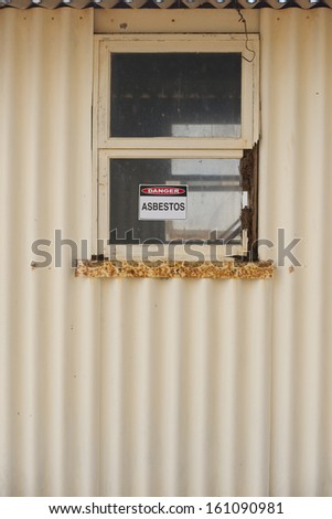 Asbestos danger warning sign on glass window at old rusty toxic contaminated building.