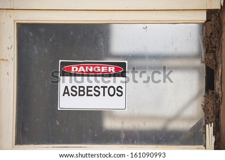 Asbestos danger warning sign on glass window at old rusty toxic contaminated building.