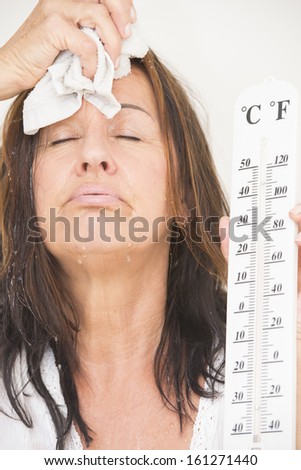 Portrait worried looking mature woman suffering from heat, high temperature, fever, with drops of sweat running down face and thermometre in hand, isolated on white.