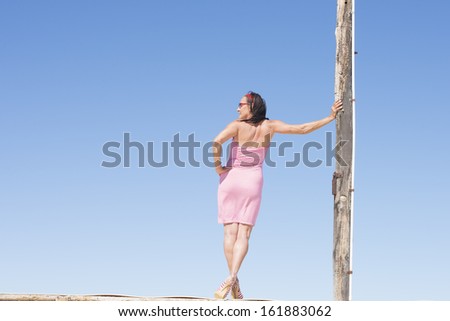 Portrait beautiful mature woman standing in leisure sexy pose on table , wearing red summer dress and high heels, with blue sky as background and copy space.
