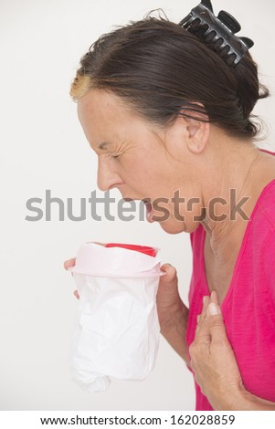Portrait sick mature woman vomiting in bag, feeling sick and ill, stressed and uncomfortable, stomach pain, isolated on white.