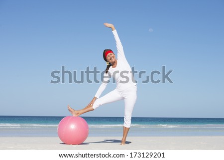 Fit and healthy attractive mature woman happy exercising with gymnastic ball at beach, enjoying active lifestyle, with ocean and sky as background and copy space.