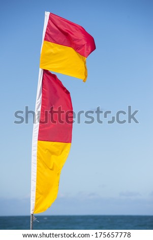 Red and yellow coloured flags of  surf live savers at Australian beach, with ocean and sky as blurred background.