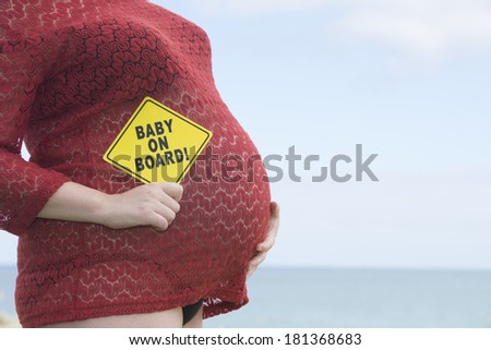 Close up of pregnant woman holding 'baby on board' sign at belly, blurred background and copy space.