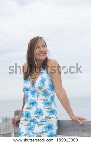 Portrait confident attractive mature woman posing friendly smiling and relaxed standing on boardwalk outdoor, with ocean and horizon as blurred background and copy space.