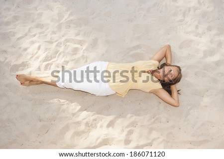 Portrait attractive mature woman lying relaxed and happy on sandy bach, smiling, hands behind neck, copy space.
