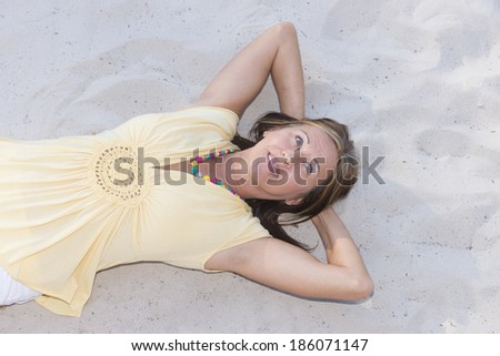 Portrait attractive relaxed mature woman lying happy smiling on sandy beach, with hands behind neck, copy space.