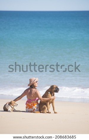Portrait beautiful mature woman sitting happy and relaxed with dogs at beach, with ocean and blue sky as background and copy space.