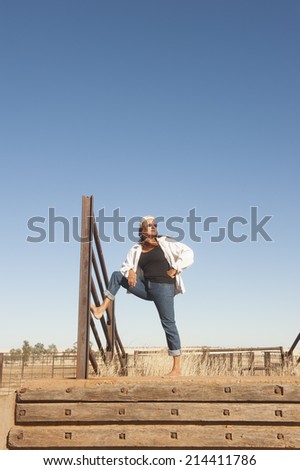 Portrait cool, relaxed attractive mature woman standing confident bare feet in rural country, wearing sunglasses, jeans and white jacket, with farm land and blue sky as background and copy space.