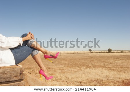 Cross legged female legs wearing sexy colorful pink high heel shoes sitting relaxed outdoor, with field and blue sky as background and copy space.