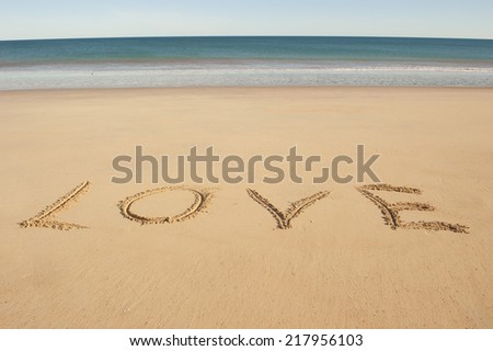 Message of Love written in capital letters in clean sandy beach at ocean, with sea and blue sky as blurred background and copy space.