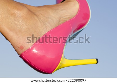 Close up of female foot in pink high heel pumps and  painful looking scratch of blister on skin, with blue sky as background and copy space.