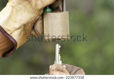 Hands in gloves with locked metal padlock and key with green blurred background.