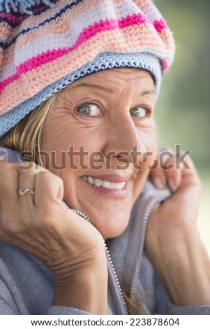 Portrait attractive mature woman with beanie cap to keep warm in winter, friendly confident smiling, blurred background outdoor.
