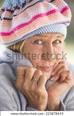 Portrait attractive mature woman with beanie hat to keep warm in winter, friendly relaxed smiling, blurred background outdoor.