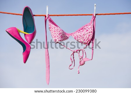 Pink Bikini top or bra hanging on clothes line after washing next to pink sexy high heel shoes, blue sky as outdoor background and copy space.