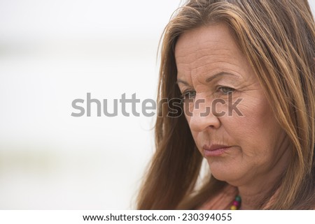 Portrait attractive mature woman with angry, stressed, sad, worried or depressed facial expression, bright outdoor background and copy space.