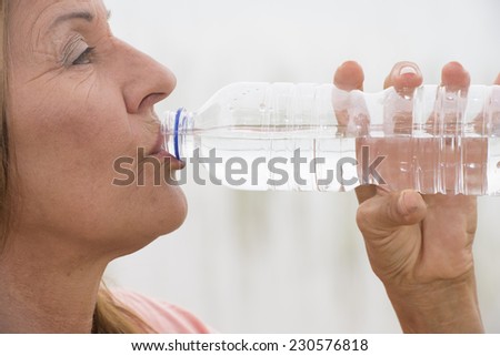 Portrait attractive mature woman relaxed happy drinking natural mineral water as refreshment after sport activity outdoor, with bright background and copy space.