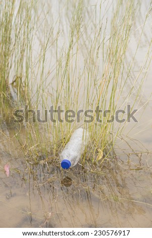 Empty plastic bottle illegal dumped and disposed, floating in water of river or lake between grass, polluting of wilderness environment, outdoor blurred background and copy space.