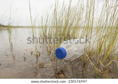 Empty plastic bottle illegal disposed, floating in water of river or lake between grass, polluting of wilderness environment, sky and horizon as outdoor blurred background and copy space.