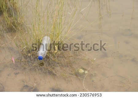Empty plastic bottle illegal dumped and disposed, floating in water of river or lake between grass, pollution of wilderness environment, outdoor blurred background and copy space.