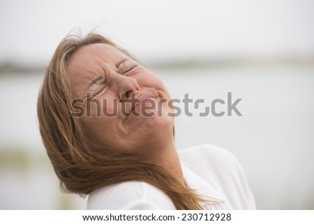 Portrait mature woman with sad, stressed, painful facial expression, crying with closed eyes outdoor, blurred background and copy space.