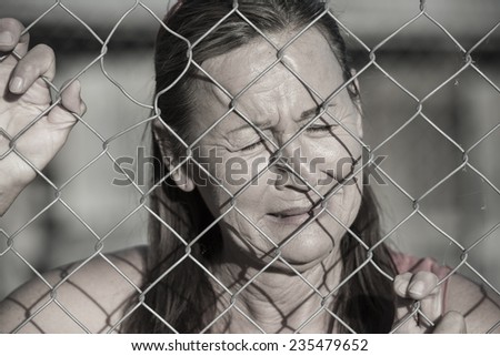 Portrait crying woman behind mesh wire fence, desperate, devastated, depressed, stressed facial expression, unhappy, closed eyes.