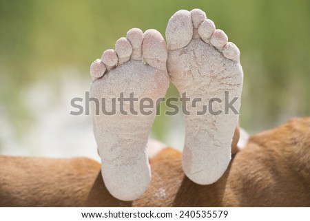 Pair of sandy bare feet soles resting outdoor with blurred background and copy space.