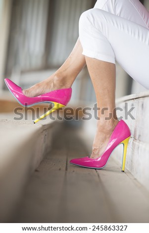 Concept close up image of woman sitting in Elegant extravagant sexy pink high heel shoes, sitting relaxed on bench, copy space, blurred background