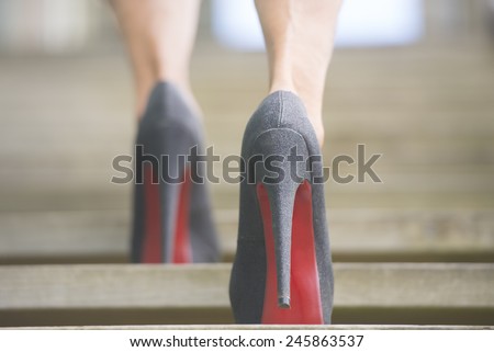 Detail close up of upward view of woman in high heel stiletto shoes walking up wooden stairs with blurred background.