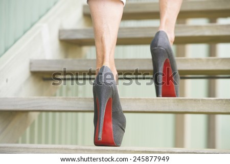 Detail close up of woman in high heel stiletto shoes walking up wooden stairs with blurred background.