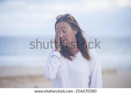 Portrait attractive mature woman with closed eyes, stressed, tired, sad, suffering from menopause, blurred background outdoor, copy space.