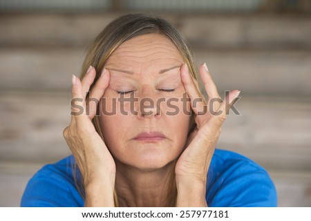 Portrait attractive mature woman with migraine headache in pain, with closed eyes, finger at forehead, blurred background.