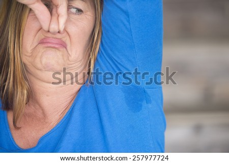 Portrait mature woman with smelly sweat perspiration under arm with wet moisture spot on shirt, blurred background, copy space.