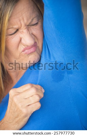 Portrait angry mature woman with sweat perspiration under arm with wet moisture spot on blue shirt, blurred background, copy space.