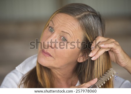 Portrait elegant attractive mature woman brushing long brunette hair, white shirt, blurred background.