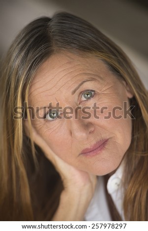Portrait attractive mature woman with serious happy confident facial expression, upward look, blurred background.