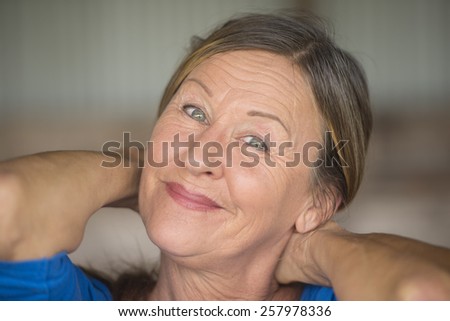 Portrait attractive mature woman with friendly positive confident facial expression, happy smiling, hands behind neck, blurred background.