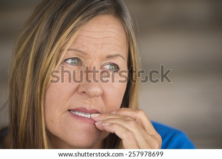 Portrait attractive mature woman with insecure nervous stressed expression, biting finger nails, blurred background.