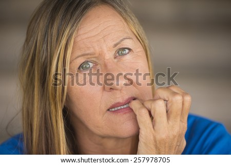 Portrait attractive mature woman with nervous stressed insecure facial expression, biting finger nails, blurred background.