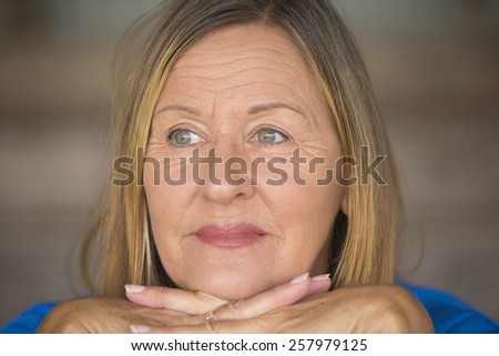 Portrait attractive mature woman with confident relaxed and happy smiling facial expression, chin rested on hands, blurred background.