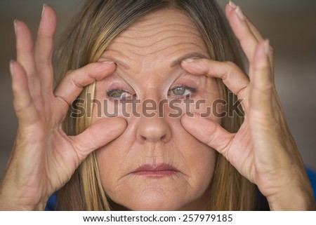 Portrait of attractive mature woman with tired and stressed facial expression, fingers keep eyes open, insomnia and headache, blurred background.