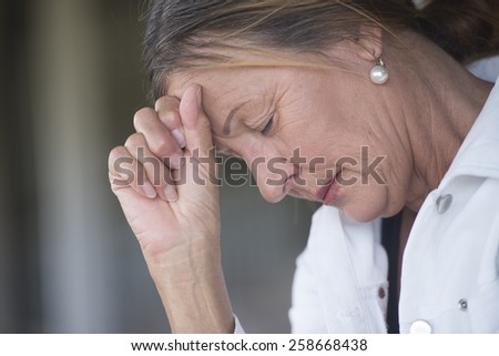 Portrait mature woman with sad, depressed, thoughtful expression, alone with closed eyes, devastated and worried, blurred background, copy space.