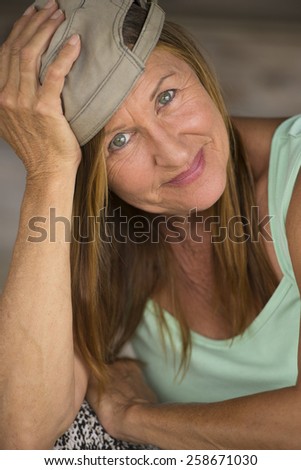 Portrait cheeky attractive active mature woman wearing green sporty top and cap, happy fit confident relaxed expression, blurred background.