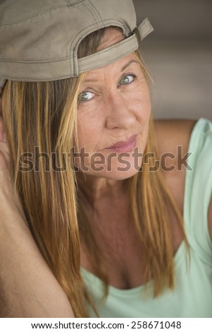 Portrait confident attractive active mature woman wearing green sporty top and cap, friendly relaxed expression, blurred background.