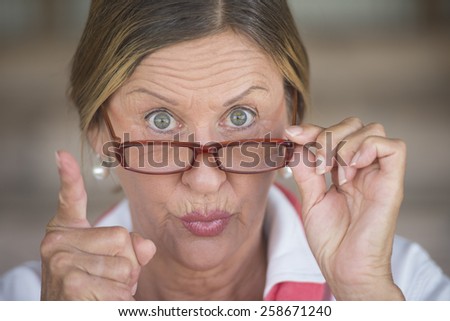 Portrait smart attractive mature business woman or dominant teacher with glasses and angry upset expression, blurred background.