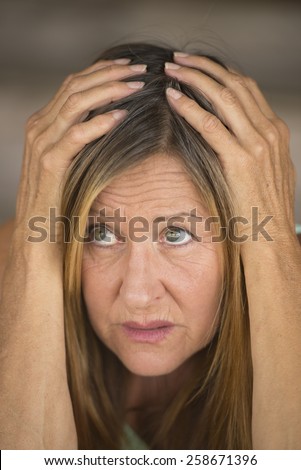 Portrait attractive mature woman, stressed, scared, unhappy frightened look, hands covering head, blurred background.