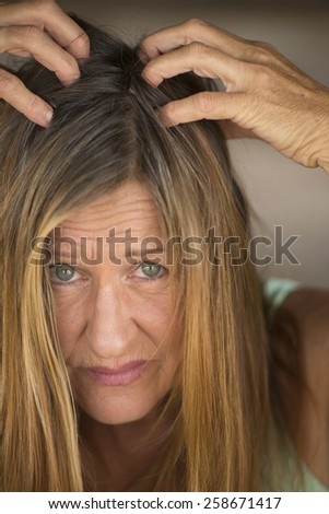 Close up Portrait attractive mature woman tearing her long brunette hair with hands, unhappy, stressed, blurred background.