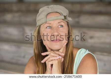 Portrait attractive fit active mature woman wearing green sporty top and cap, thoughtful relaxed confidence, chin resting on hands, blurred background.